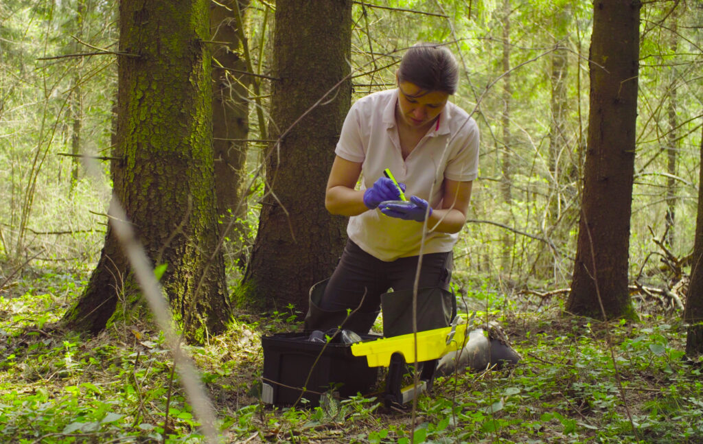 Woman scientist ecologist in the forest marking the petry dish with samples of the moss
